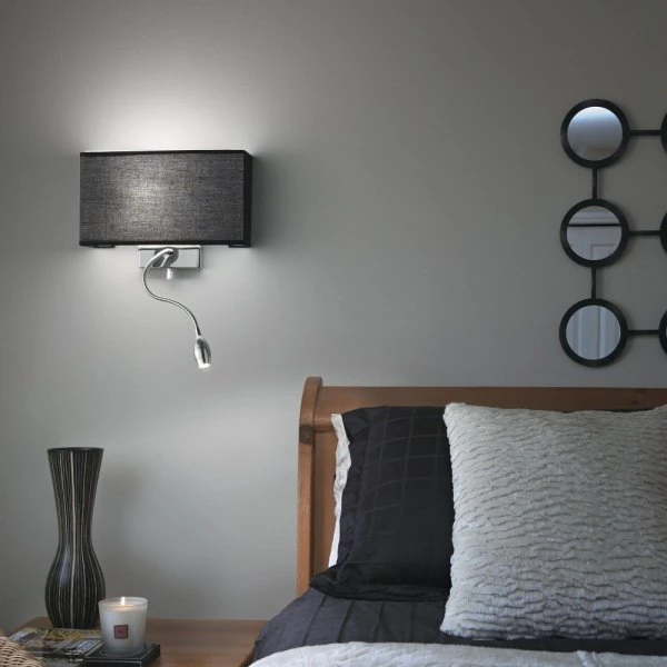 Black wall lamp with LED reading lamp turned on next to the bed